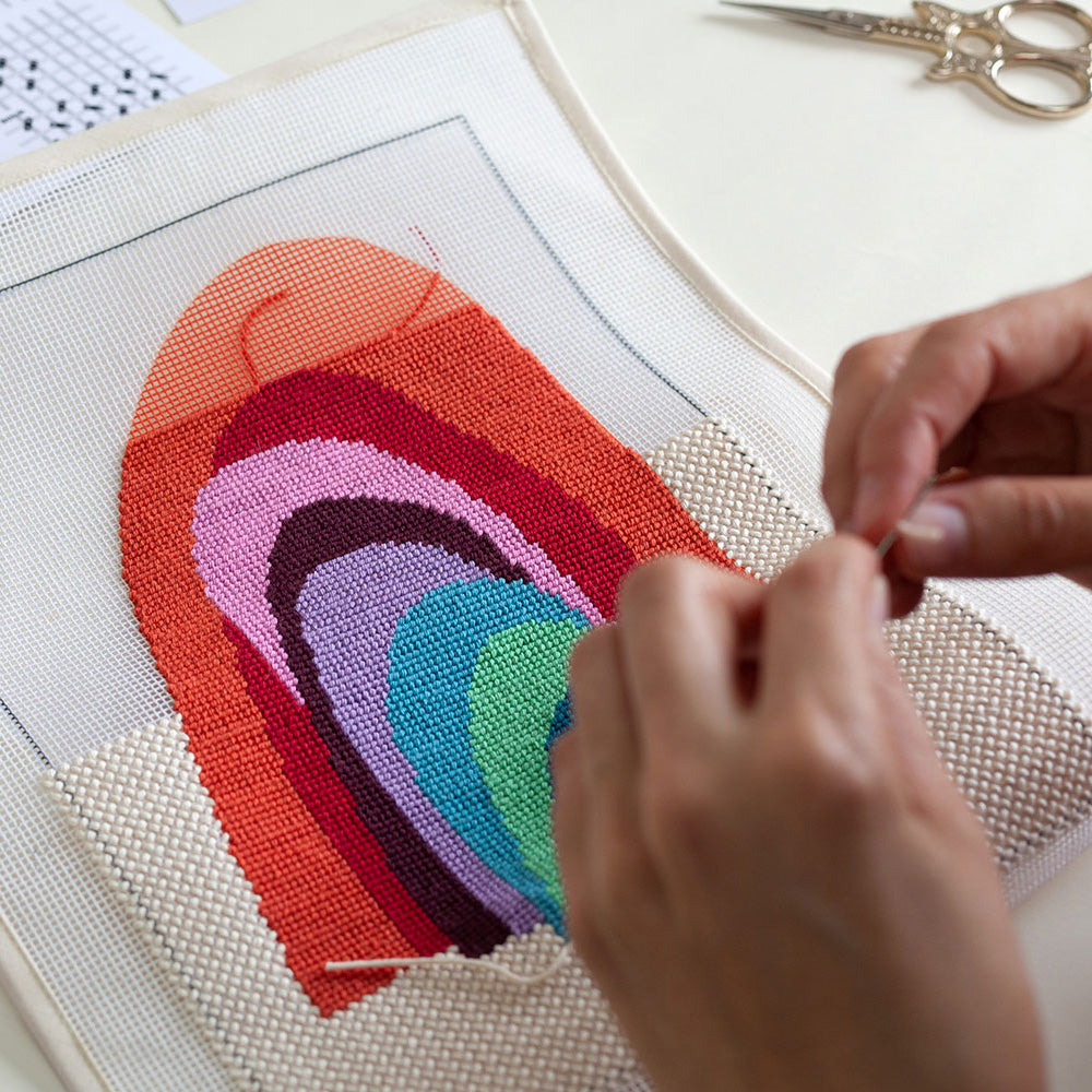 hands stitching needlepoint with illustration of rainbow