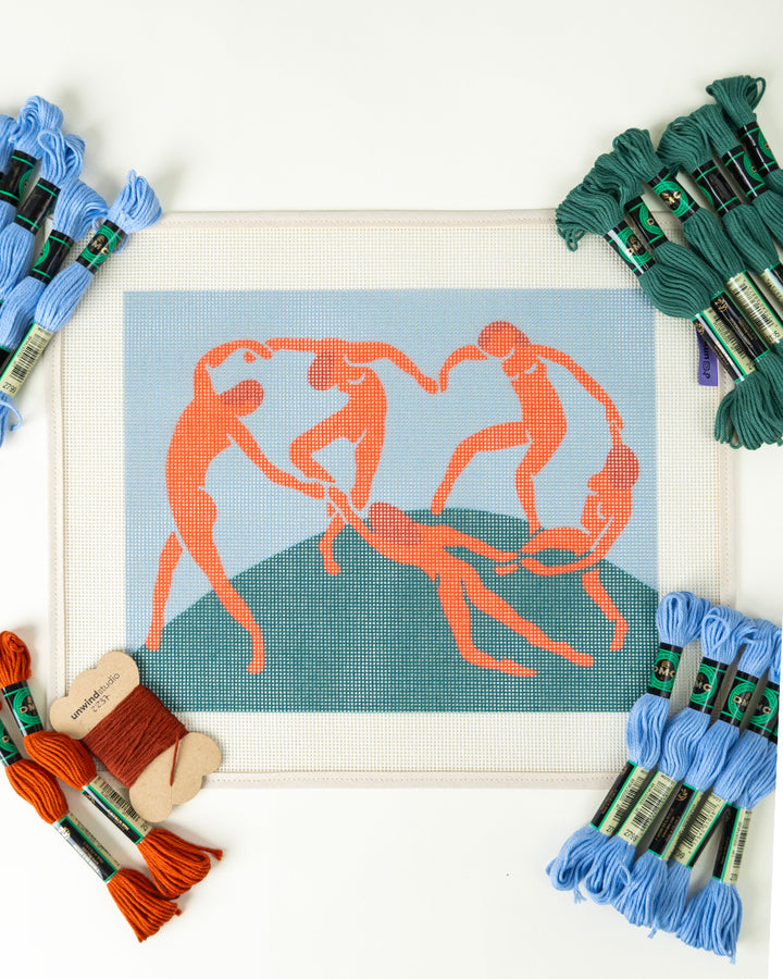 Cross-stitching project with orange figures on a blue background, surrounded by embroidery threads.