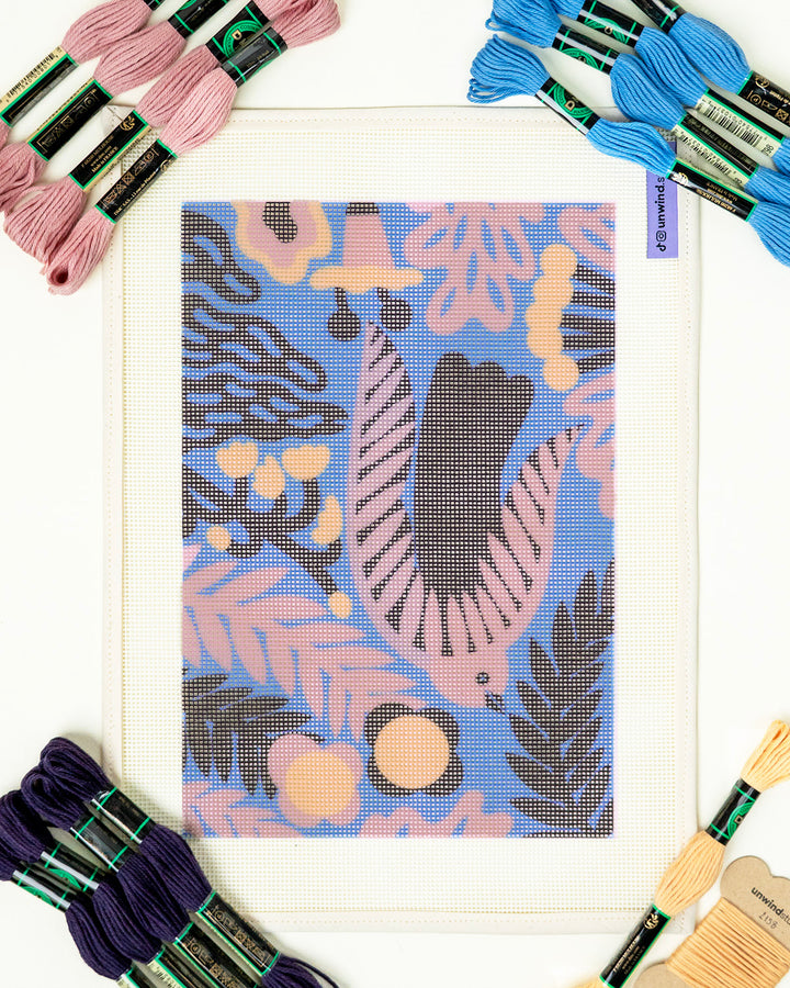 needlepoint kit with a pre-printed design of a sloth and plants, surrounded by embroidery threads.