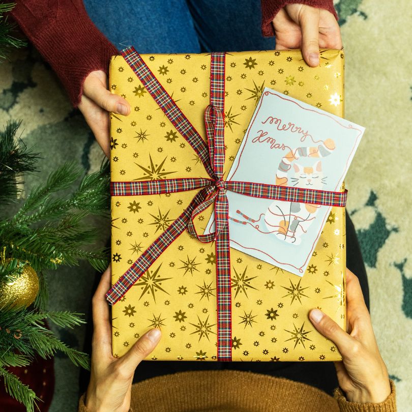 a gift box being offered to a friend with a card and inside it is a needlepoint kit