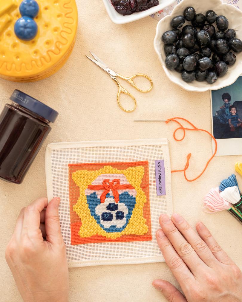 Blueberry Jam-inspired needlepoint coaster kit displayed on a table with jam and blueberries.