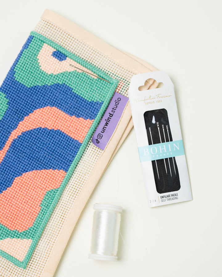 Flat view of the Bohin France Sewing Needles by unwind studio placed side by side with a needlepoint canvas