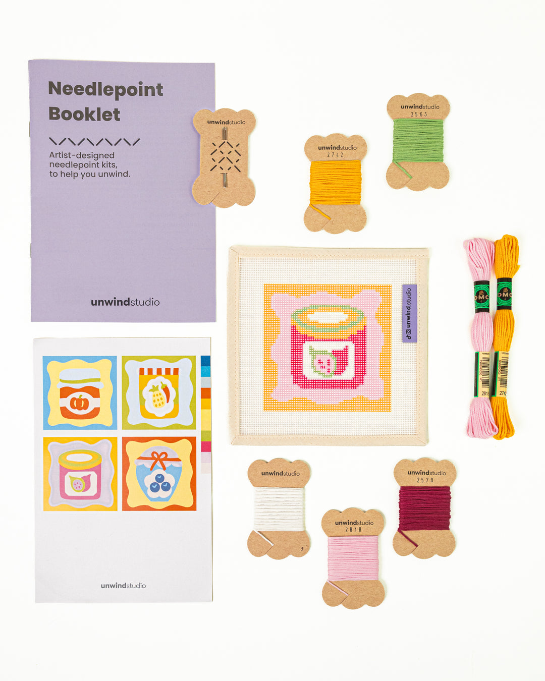 Top-down view of the Fig Jam Coaster needlepoint kit including canvases, DMC Soft Cotton thread, flyer, and a instructional booklet.