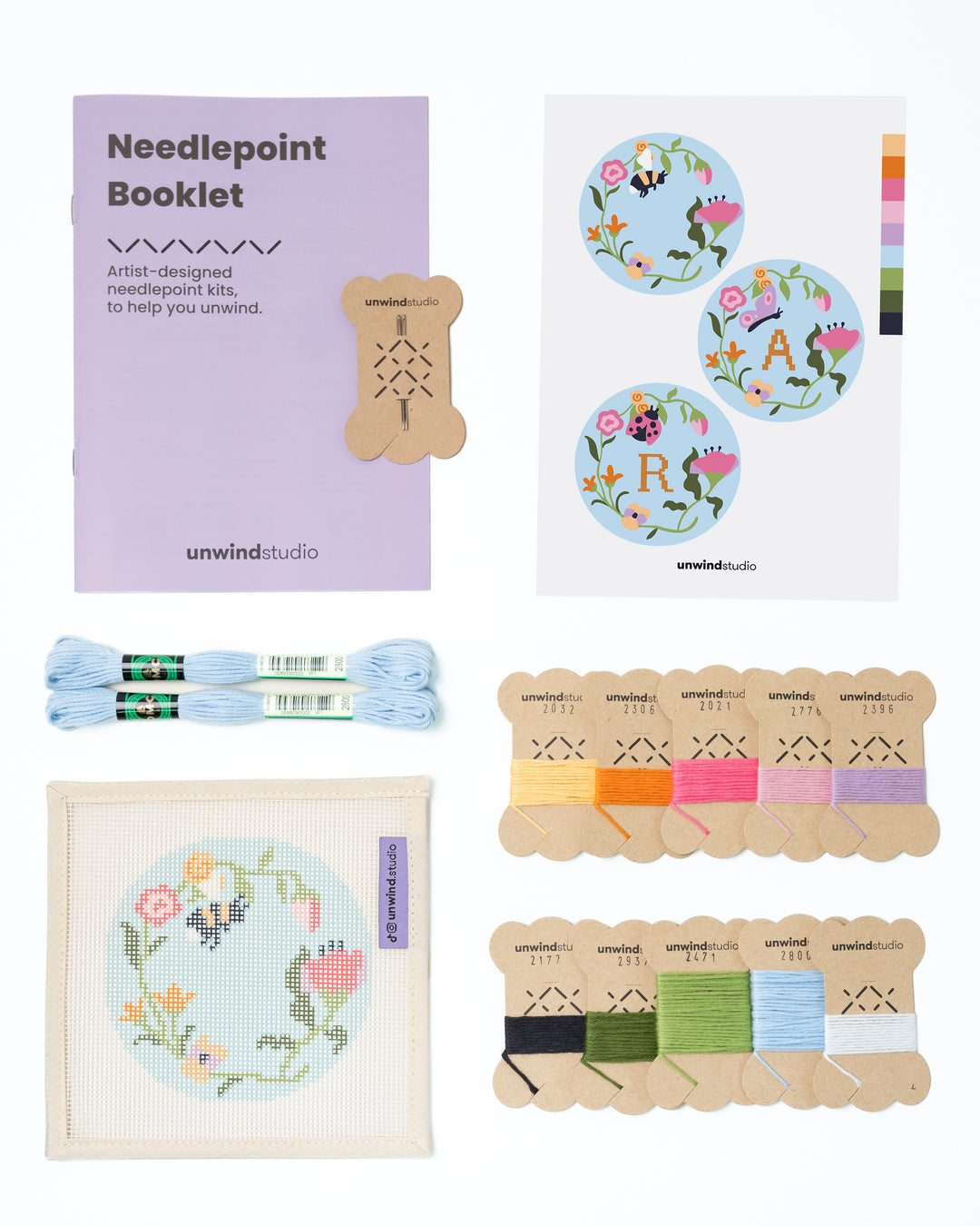 Flat view of the Garden Bee Needlepoint Ornament by Unwind Studio with an instructional booklet, needle, dmc soft cotton threads and a graphic flyer
