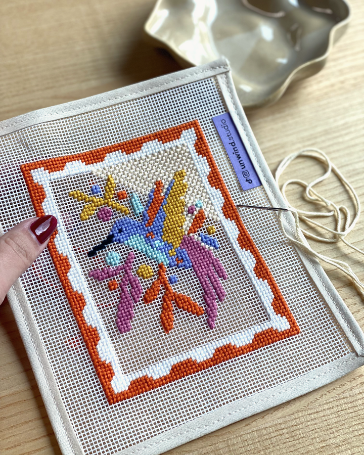 Hummingbird needlepoint canvas kit with colorful bird design and orange border, stitched on white mesh canvas.