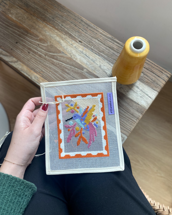 Hummingbird needlepoint canvas in progress with needle and thread.