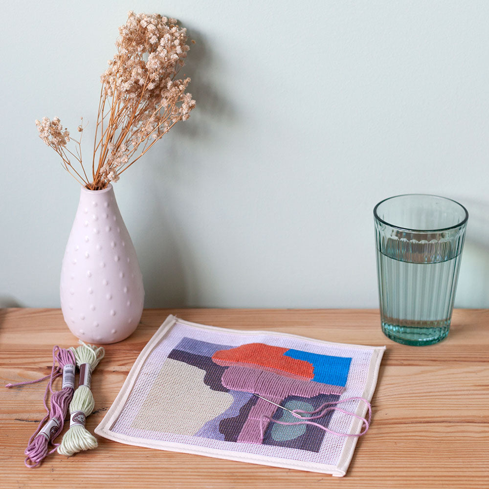 needlepoint canvas set on table next to glass of water and vase with flowers