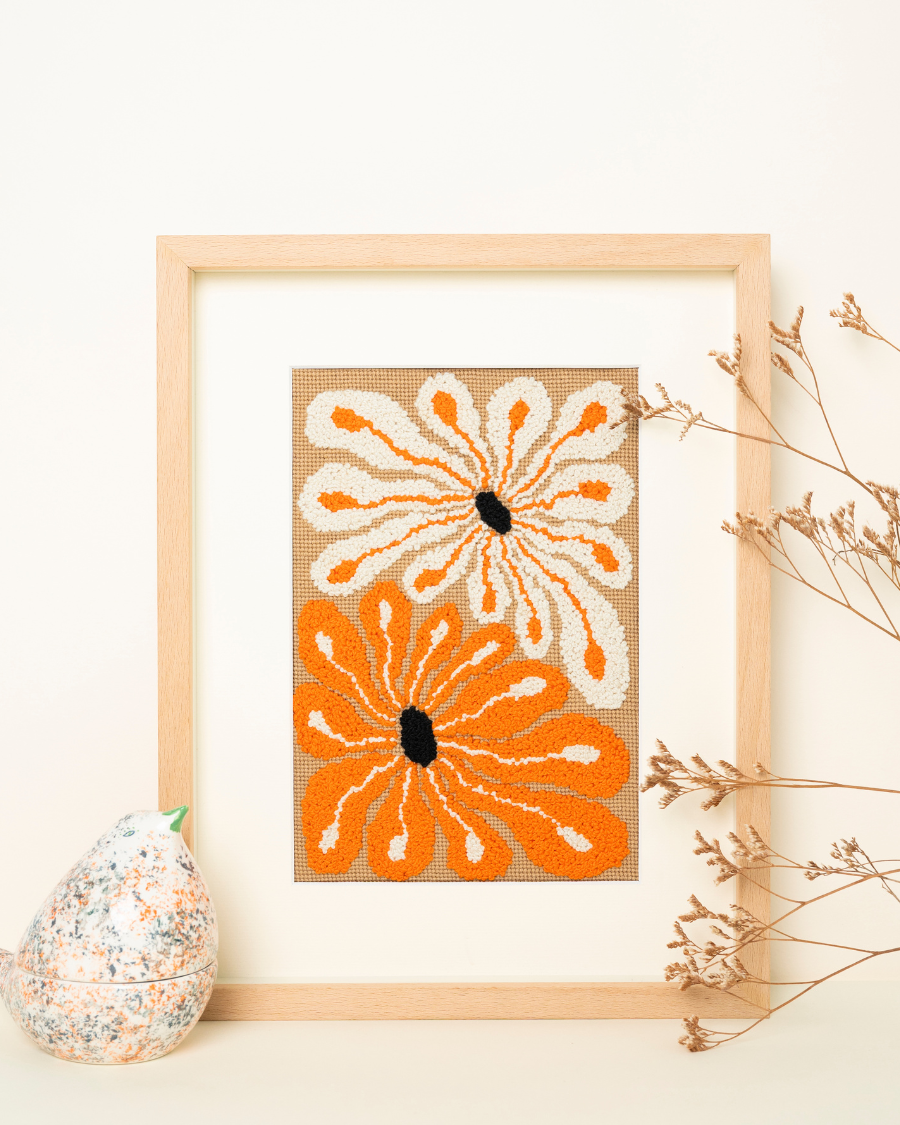 Juanita Needlepoint Kit by unwind studio placed on a wood frame with decorative elements like a ceramic bird and dry flowers