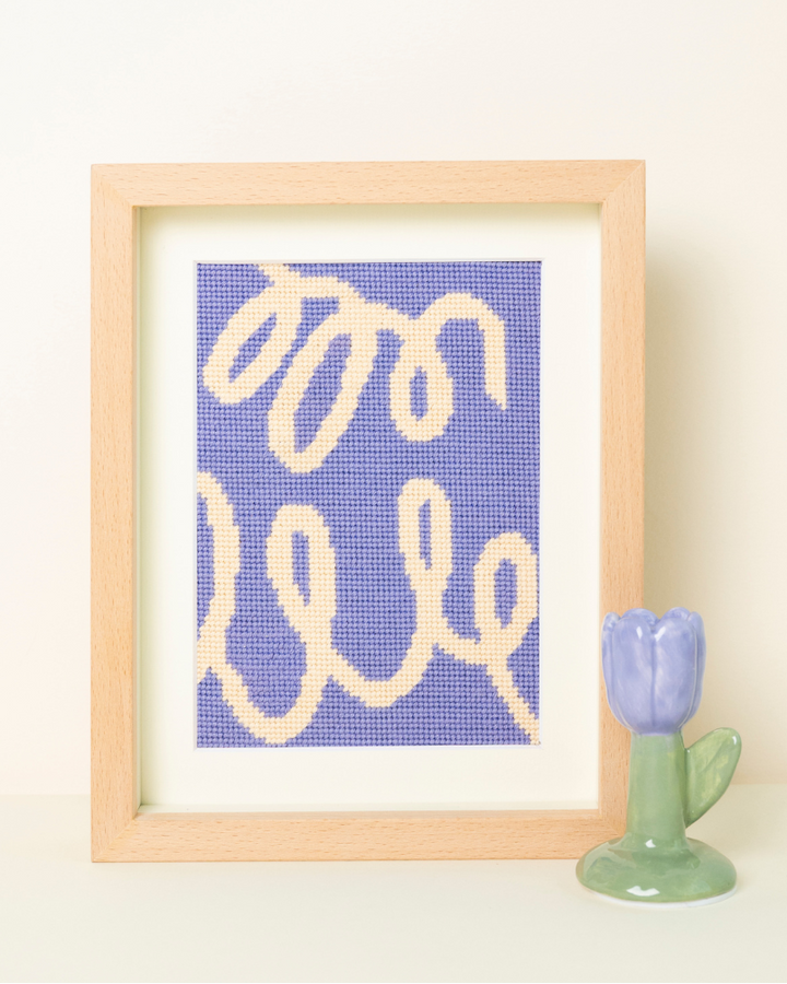 Olele Needlepoint Kit by Unwind Studio placed on a wood frame with a ceramic tulip next to it.