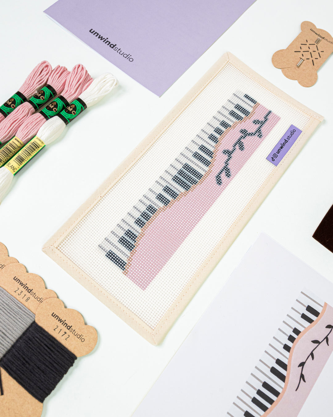 Close-up, diagonal view of the Piano Forte needlepoint canvas and materials, showcasing the soft pastel color palette and high-quality needlework supplies.