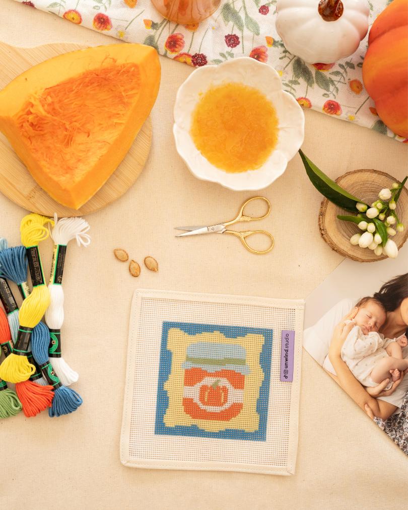 Pumpkin Jam-inspired needlepoint coaster kit displayed on a table with matching objects.