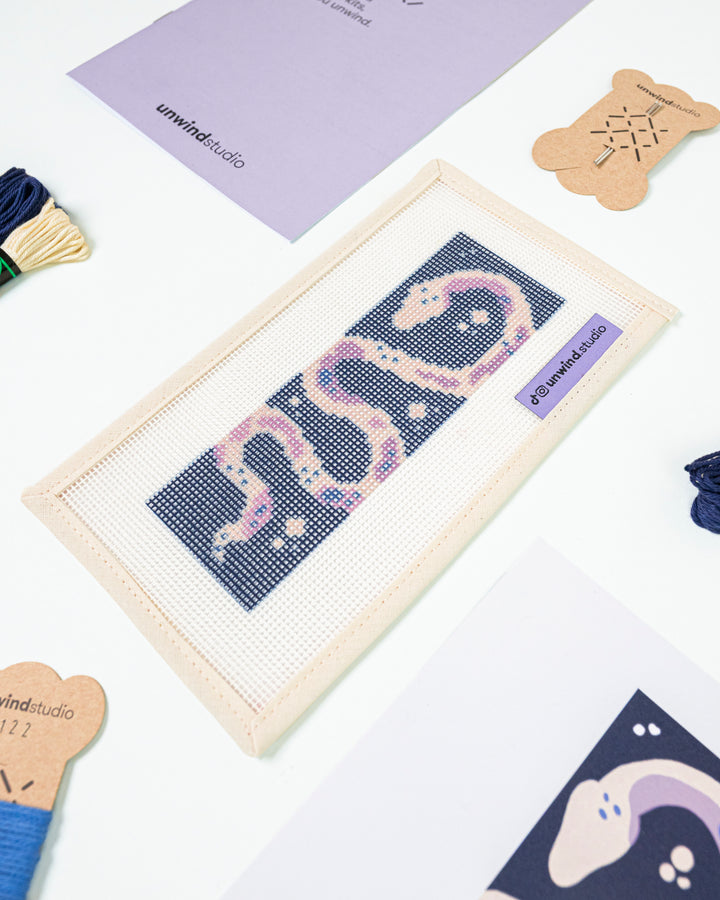 Close-up, diagonal view of The Serpent's Tale needlepoint canvas and materials, showcasing the bold color palette and high-quality needlework supplies.