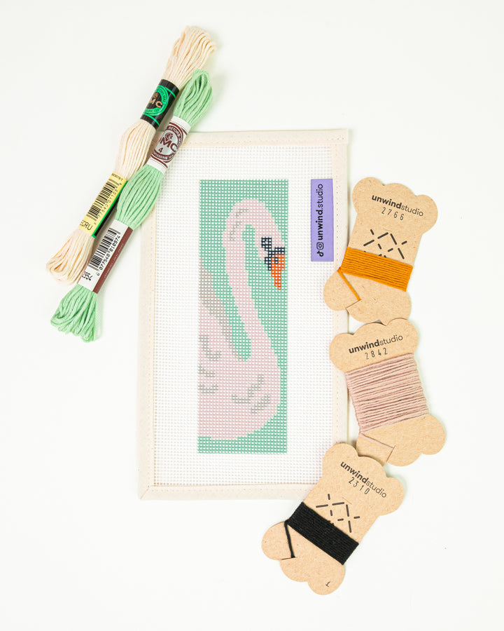 The White Swan needlepoint bookmark kit with a graceful swan design on a mint green background, surrounded by kit DMC Soft Cotton Threads.