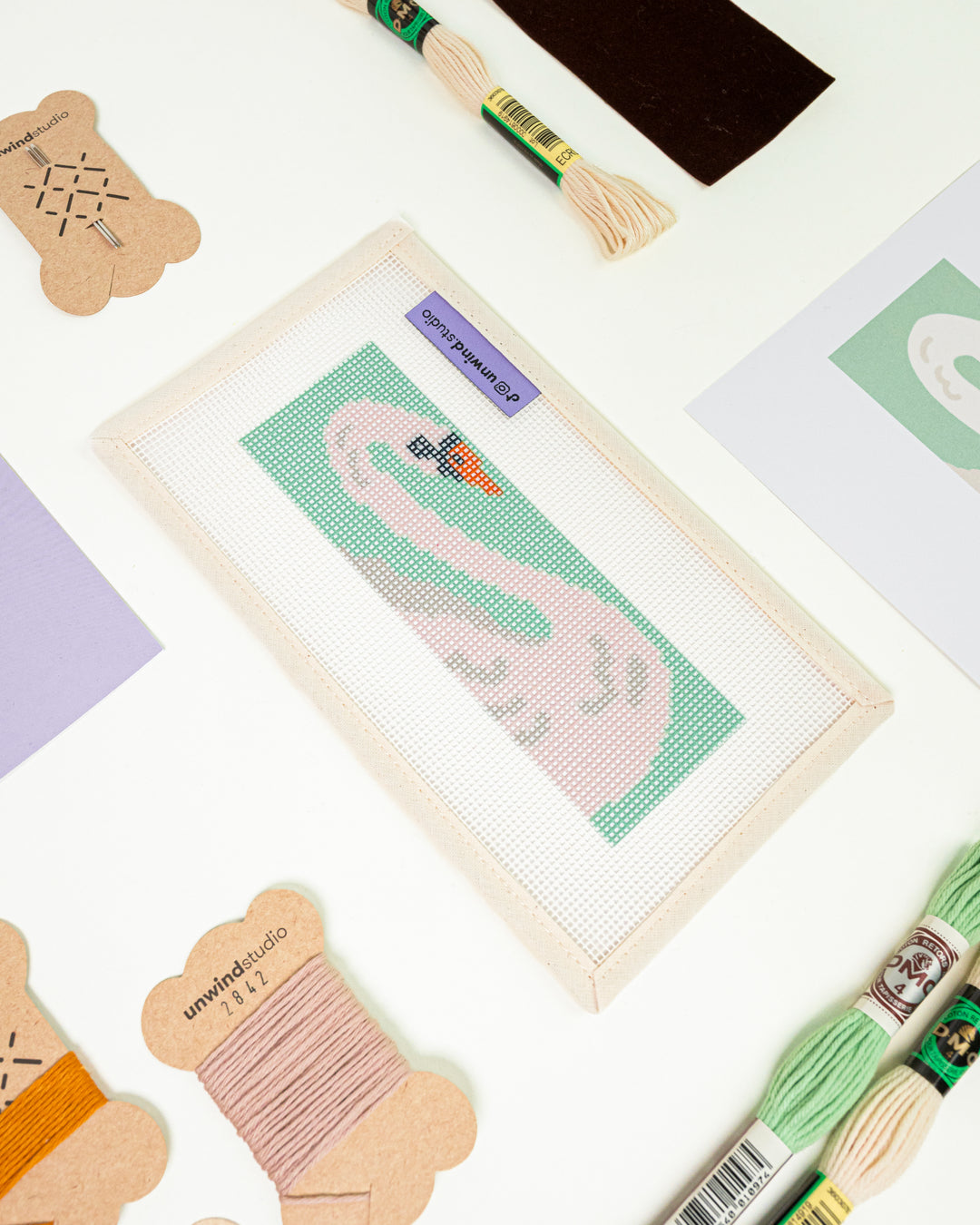 Close-up, diagonal view of The White Swan needlepoint canvas and materials, showcasing the soft pastel color palette and high-quality needlework supplies.