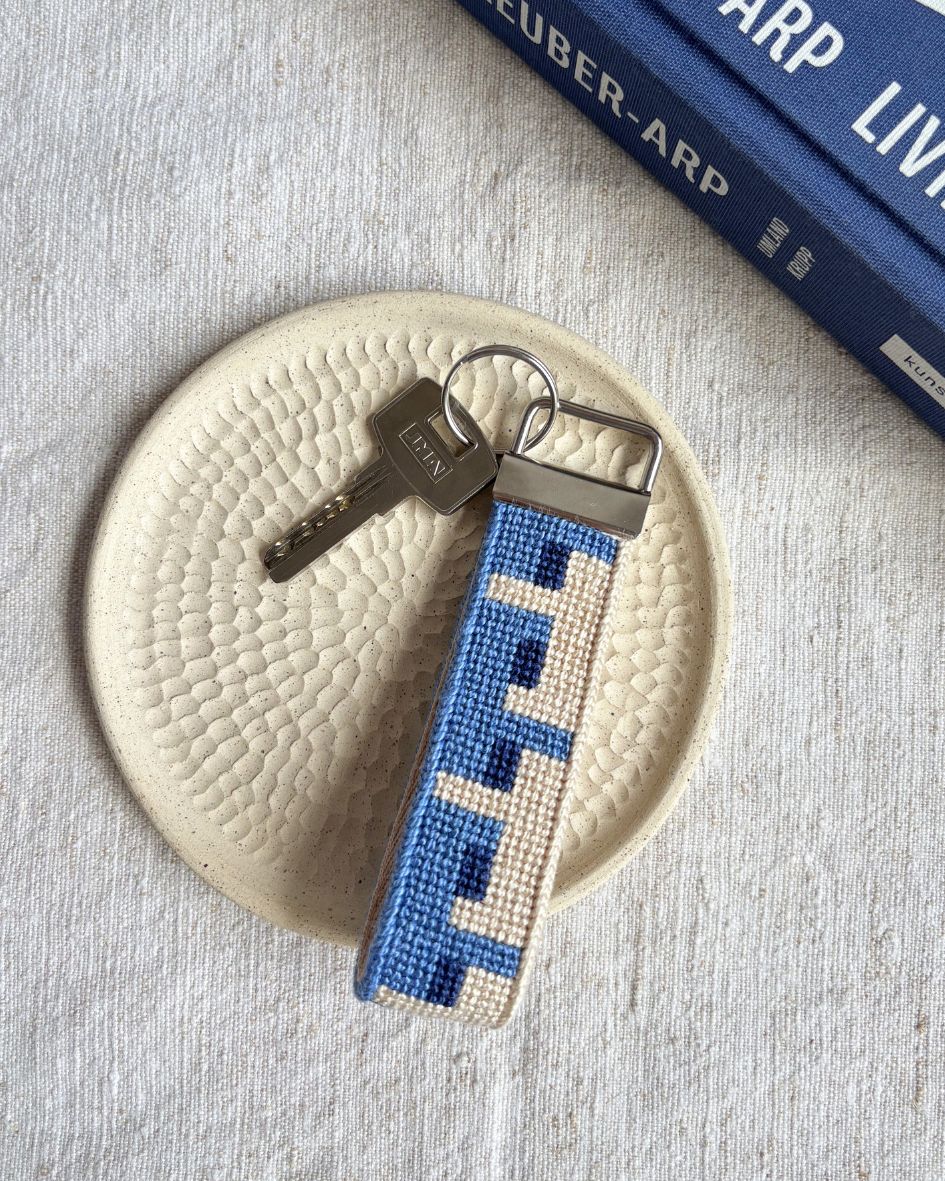 Batik Key Fob needlepoint kit placed on top of a ceramic plate and a matching blue book beside it
