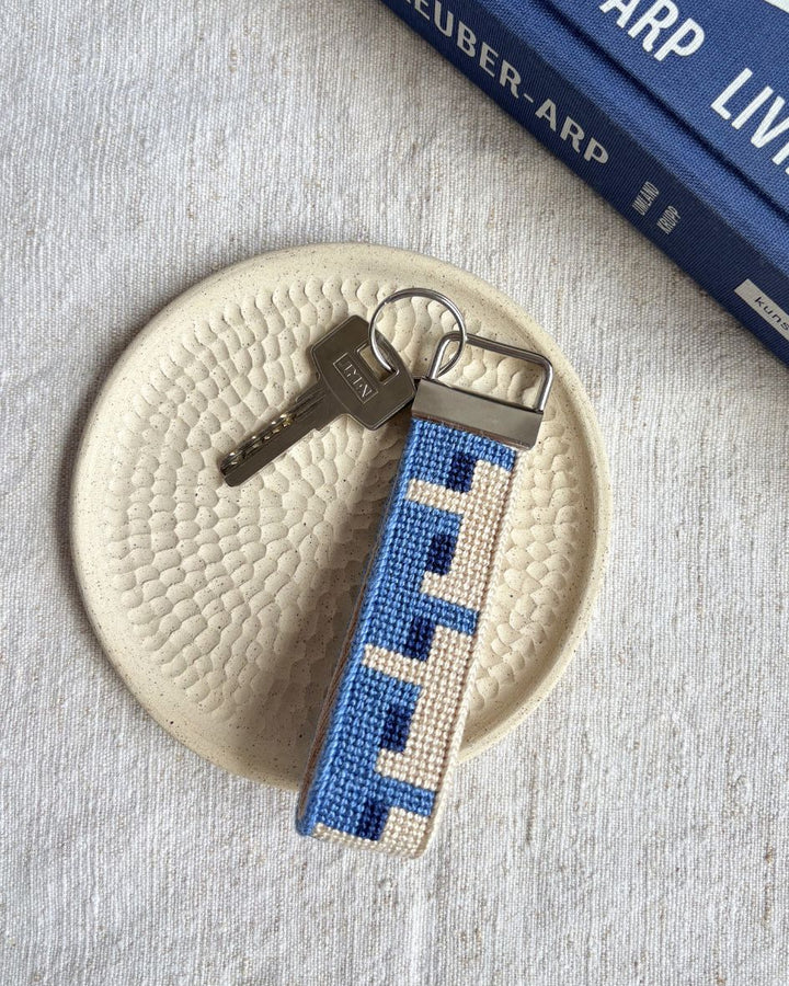 Batik Key Fob needlepoint kit placed on top of a ceramic plate and a matching blue book beside it

