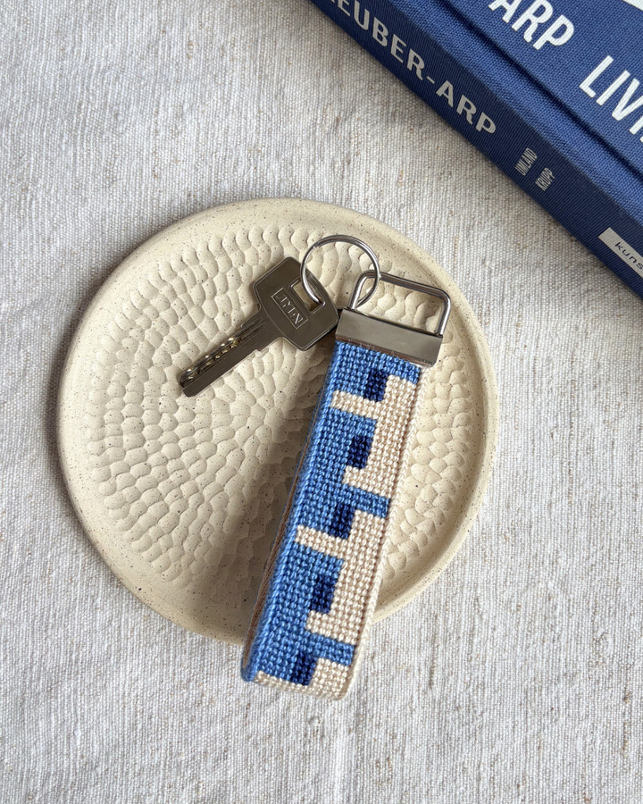 Batik Key Fob needlepoint kit placed on top of a ceramic plate and a matching blue book beside it