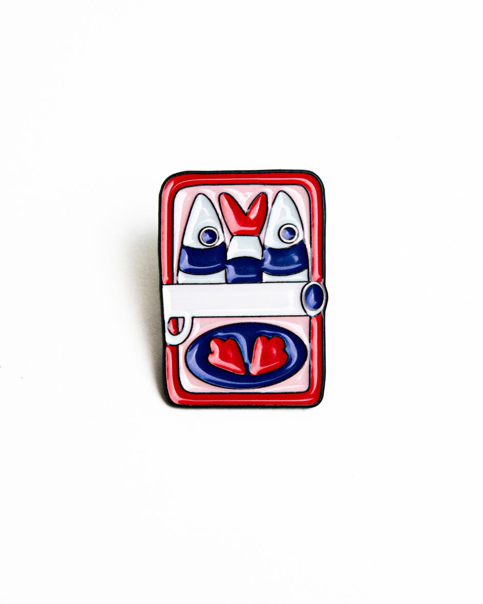 up-close shot of the unwind studio needle minder can of sardines magnet (enamel pin) in a red, white, pink and blue tones.

