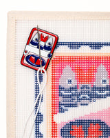 close shot of unwind studio needle minder can of sardines magnet placed on a matching can of sardines  stamp needlepoint canvas with a needle with a white thread on top.