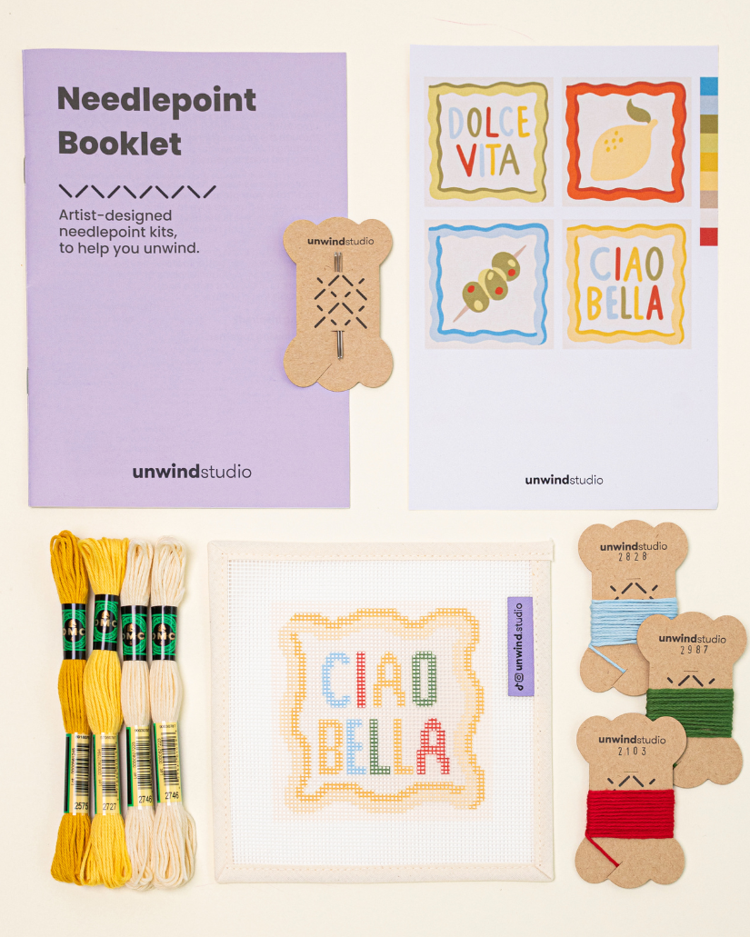 Top-down view of theciao bella Coaster set needlepoint kit including canvases, DMC Soft Cotton thread, flyer, and an instructional booklet.


