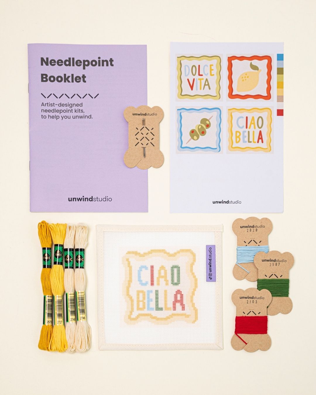 Top-down view of theciao bella Coaster set needlepoint kit including canvases, DMC Soft Cotton thread, flyer, and an instructional booklet.
