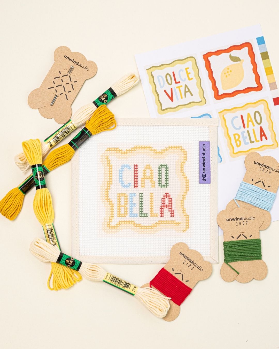 flat lay of the ciao bella needlepoint coaster paired with the matching DMC Soft Cotton Threads, needle and graphic flyer.