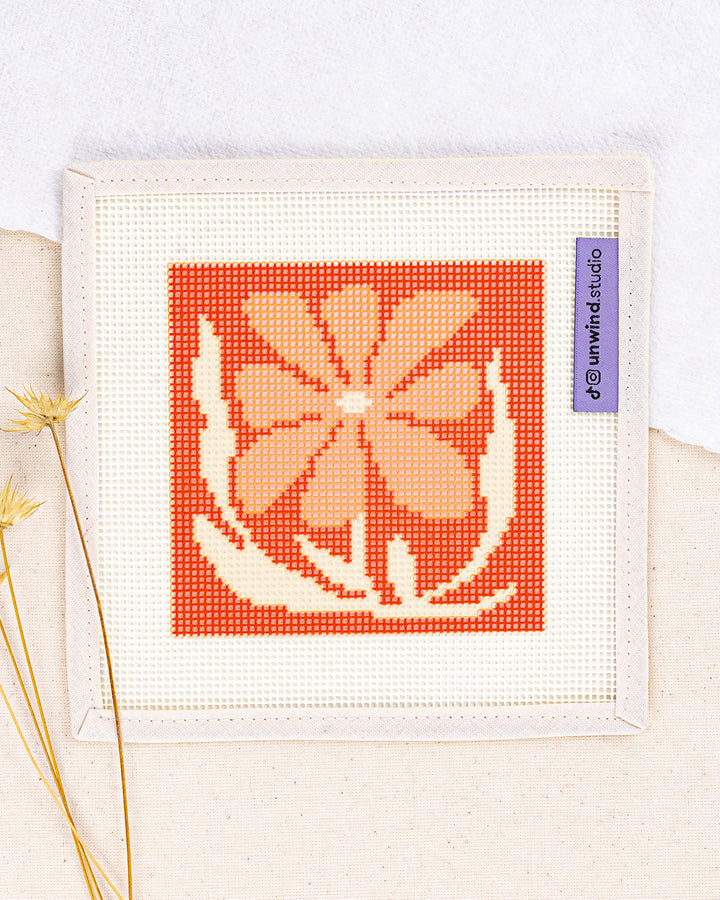Coral Bloom Coaster needlepoint kit by diana pereira: printed canvas of orange flowers on red, framed with dried twigs