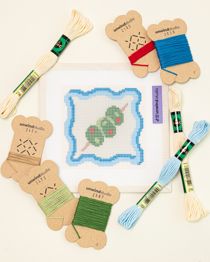 flat lay shot of the unwind studio dirty martini needlepoint coaster with bold colorful threads.