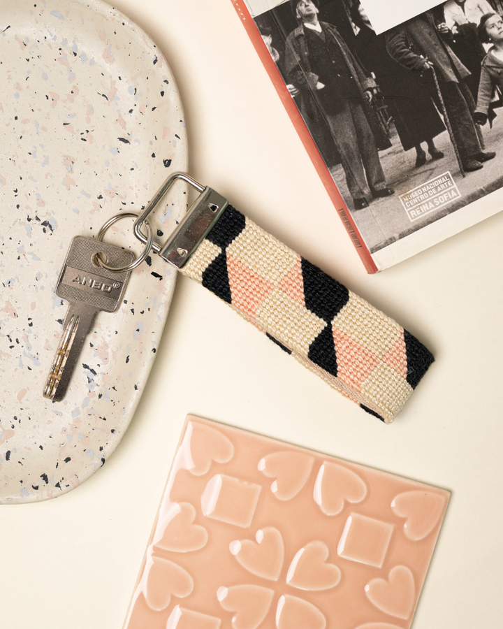 Echo Key Fob needlepoint kit place on a table with matching light pink decor elements and a book