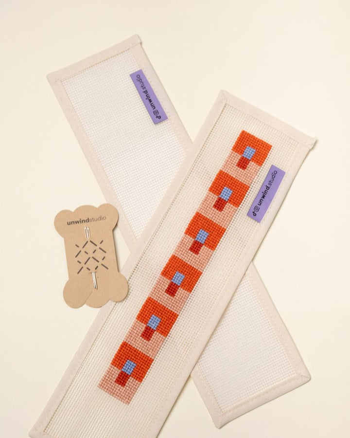 flat view of the Focus Key Fob Needlepoint Kit with blank canvas, a finished canvas and a pair of needles
