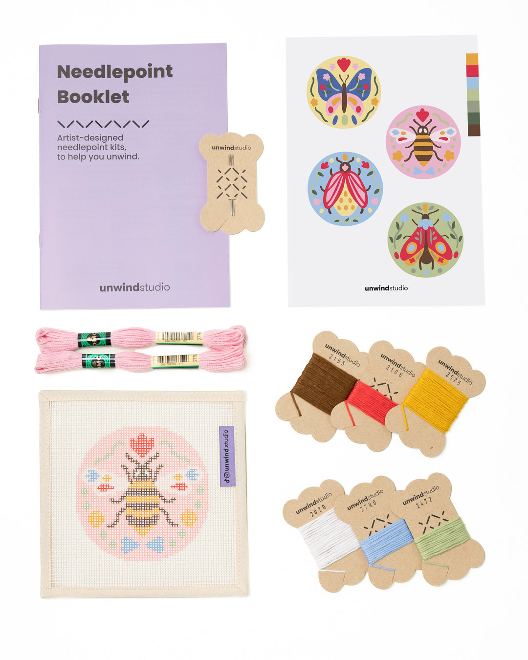 Flat view of the Folk Bee Needlepoint Ornament by Unwind Studio with an instructional booklet, needle, dmc soft cotton threads and a graphic flyer