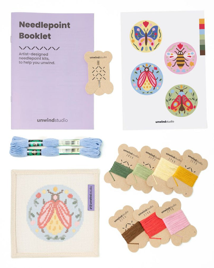Flat view of the Folk beetle Needlepoint Ornament by Unwind Studio with an instructional booklet, needle, dmc soft cotton threads and a graphic flyer
