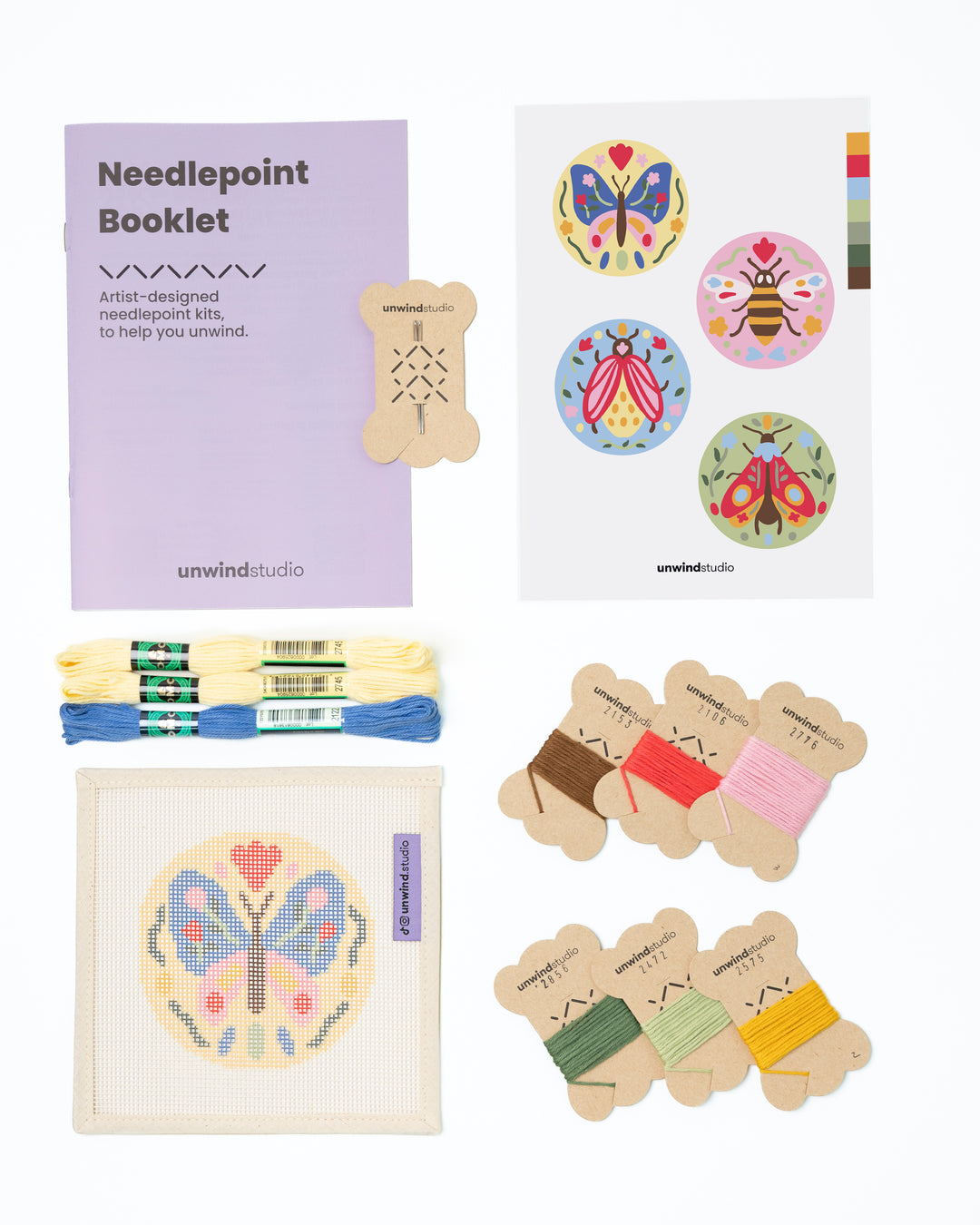 Flat view of the Folk Butterfly Needlepoint Ornament by Unwind Studio with an instructional booklet, needle, dmc soft cotton threads and a graphic flyer