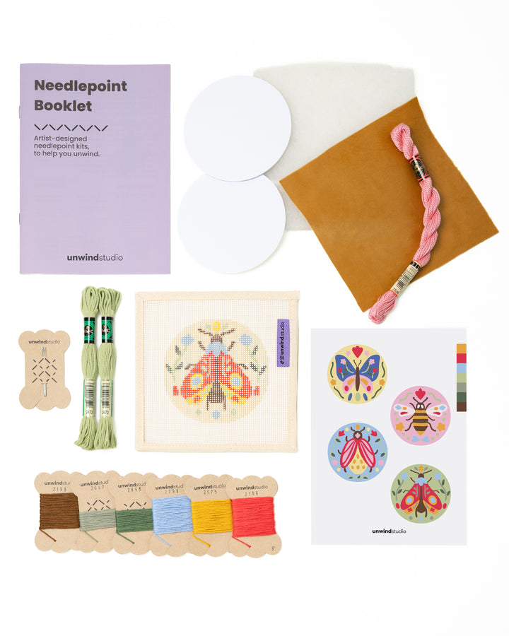 Flat view of the Folk Moth  Needlepoint Ornament by Unwind Studio with everything that comes with the kit: an instructional booklet, needle, dmc soft cotton threads, finishing materials and a graphic flyer

