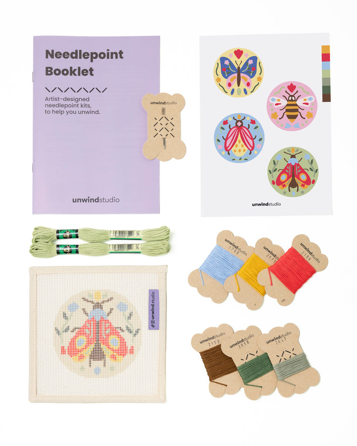 Flat view of the Folk Moth  Needlepoint Ornament by Unwind Studio with an instructional booklet, needle, dmc soft cotton threads and a graphic flyer