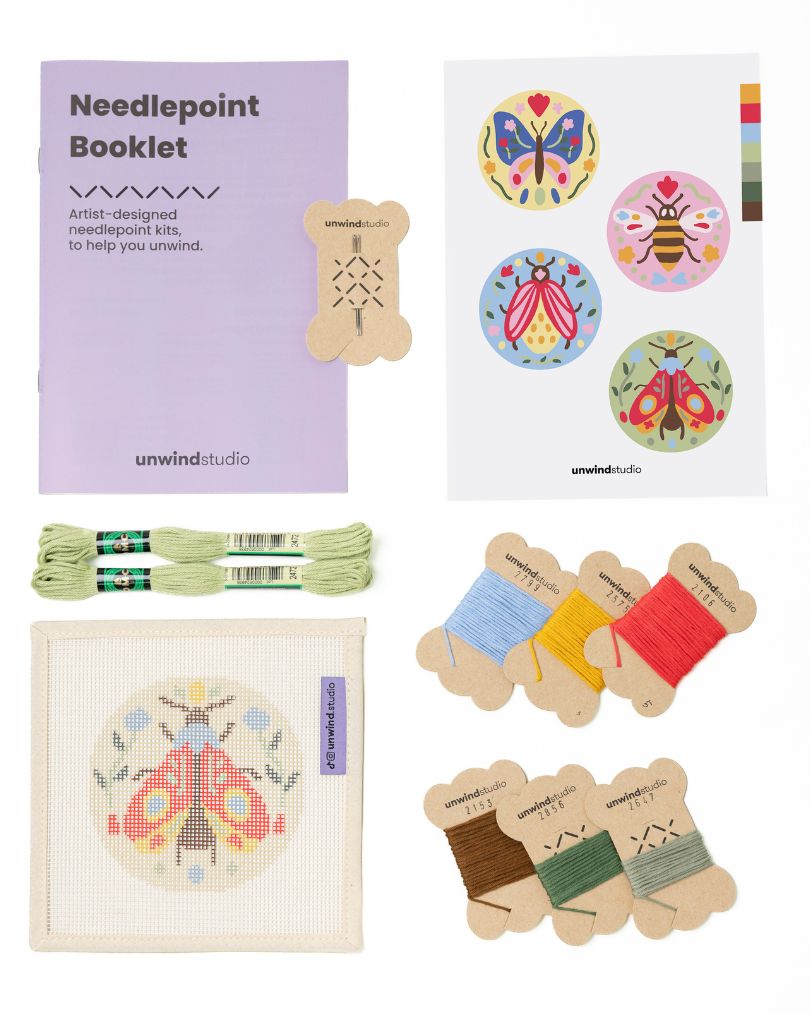 Flat view of the Folk moth Needlepoint Ornament by Unwind Studio with an instructional booklet, needle, dmc soft cotton threads and a graphic flyer
