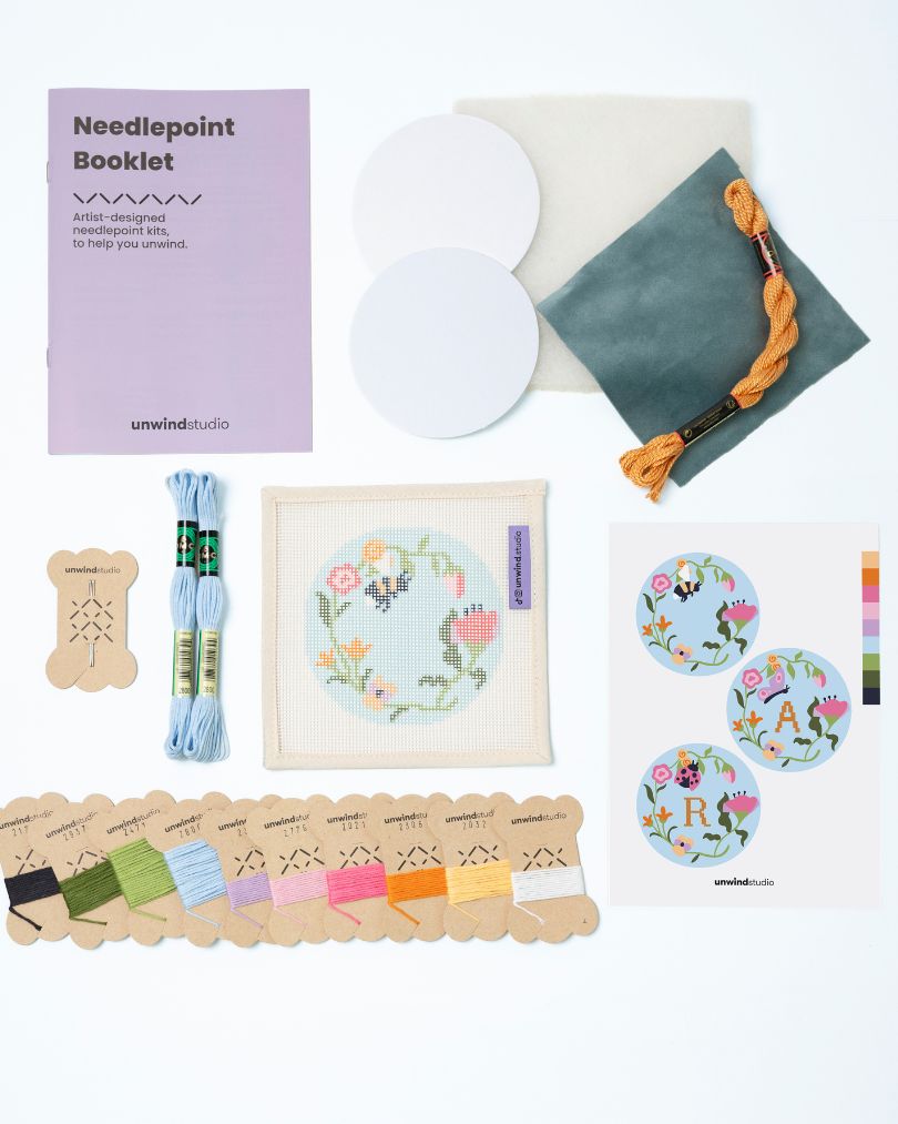  Flat view of the Garden bee Needlepoint Ornament by Unwind Studio with everything that comes with the kit: an instructional booklet, needle, dmc soft cotton threads, finishing materials and a graphic flyer
