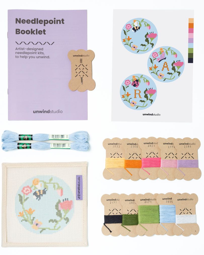 Flat view of the Garden bee Needlepoint Ornament by Unwind Studio with an instructional booklet, needle, dmc soft cotton threads and a graphic flyer
