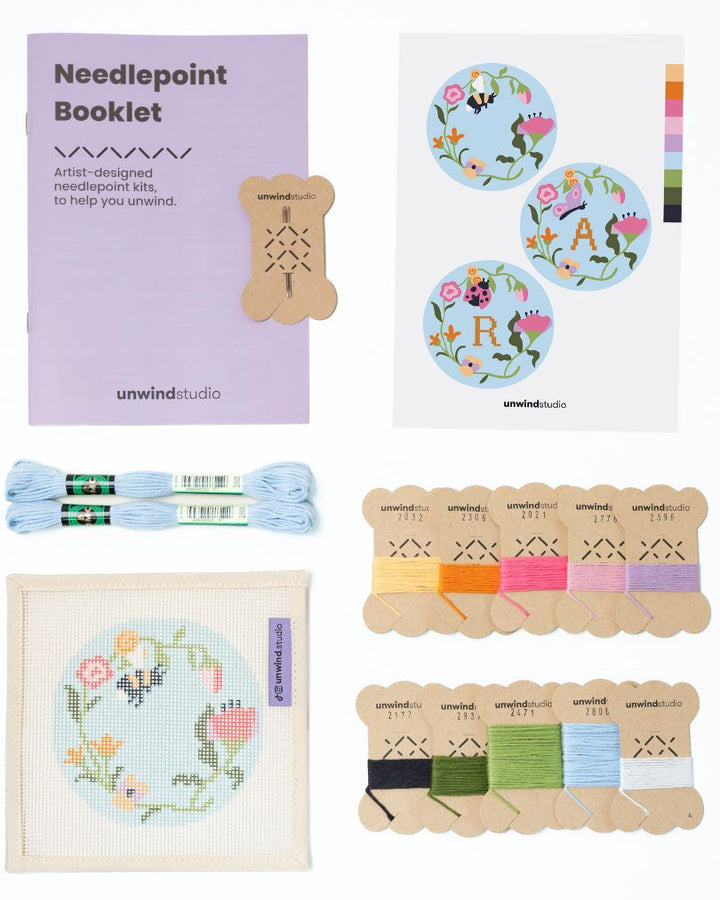 Flat view of the Garden bee Needlepoint Ornament by Unwind Studio with an instructional booklet, needle, dmc soft cotton threads and a graphic flyer
