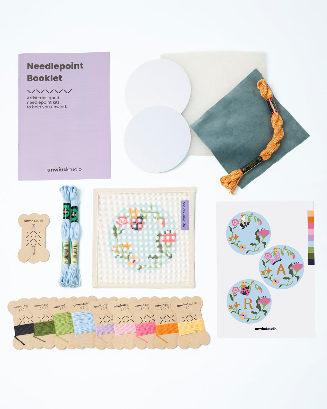Flat view of the Garden ladybug Needlepoint Ornament by Unwind Studio with everything that comes with the kit: an instructional booklet, needle, dmc soft cotton threads, finishing materials and a graphic flyer

