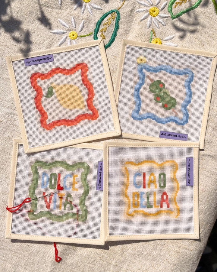 Flat lay of the four needlepoint coasters as part of the italian summer coaster set in a sunny display.