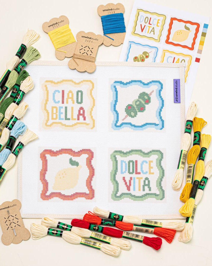 flat lay of Unwind Studio italian summer coaster set paired with all the colorul DMC Soft Cotton threads that are part of this needlepoint kit.