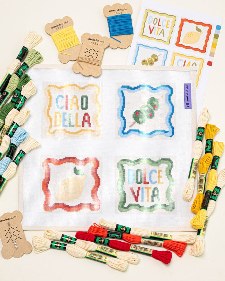 flat lay of Unwind Studio italian summer coaster set paired with all the colorul DMC Soft Cotton threads that are part of this needlepoint kit.