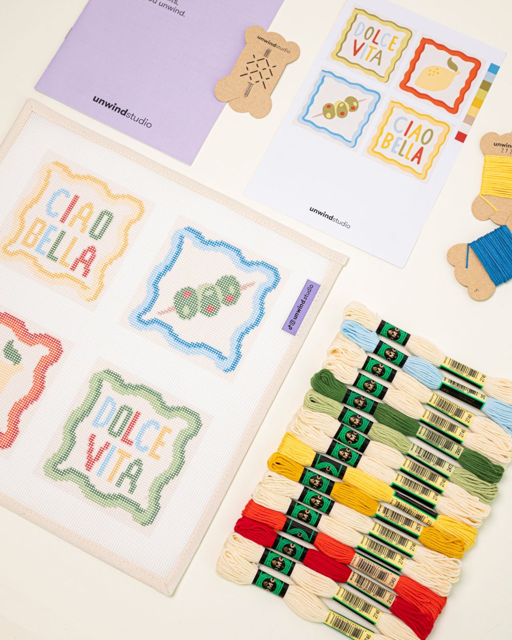diagonal flat lay of the italian summer coaster set (4 coasters) with graphic flyer,  instructional booklet and DMC Soft Cotton Threads 