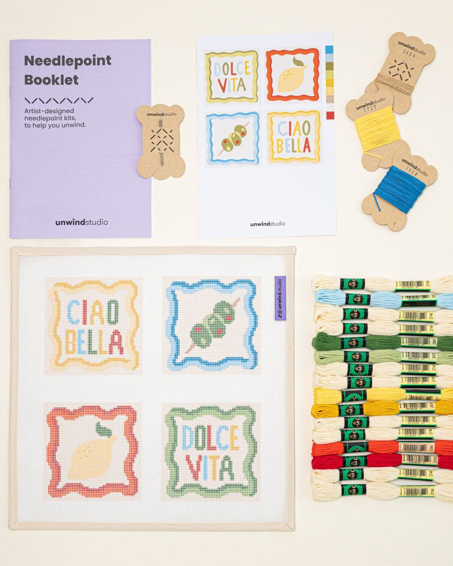Top-down view of the italian summer Coaster set needlepoint kit including canvases, DMC Soft Cotton thread, flyer, and a instructional booklet.