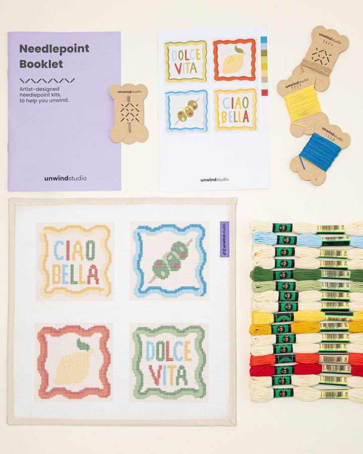 Top-down view of the italian summer Coaster set needlepoint kit including canvases, DMC Soft Cotton thread, flyer, and a instructional booklet.