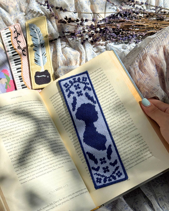 finished jane austen needlepoint bookmark placed on top of a open book, with new regency bookmarks finished in the background