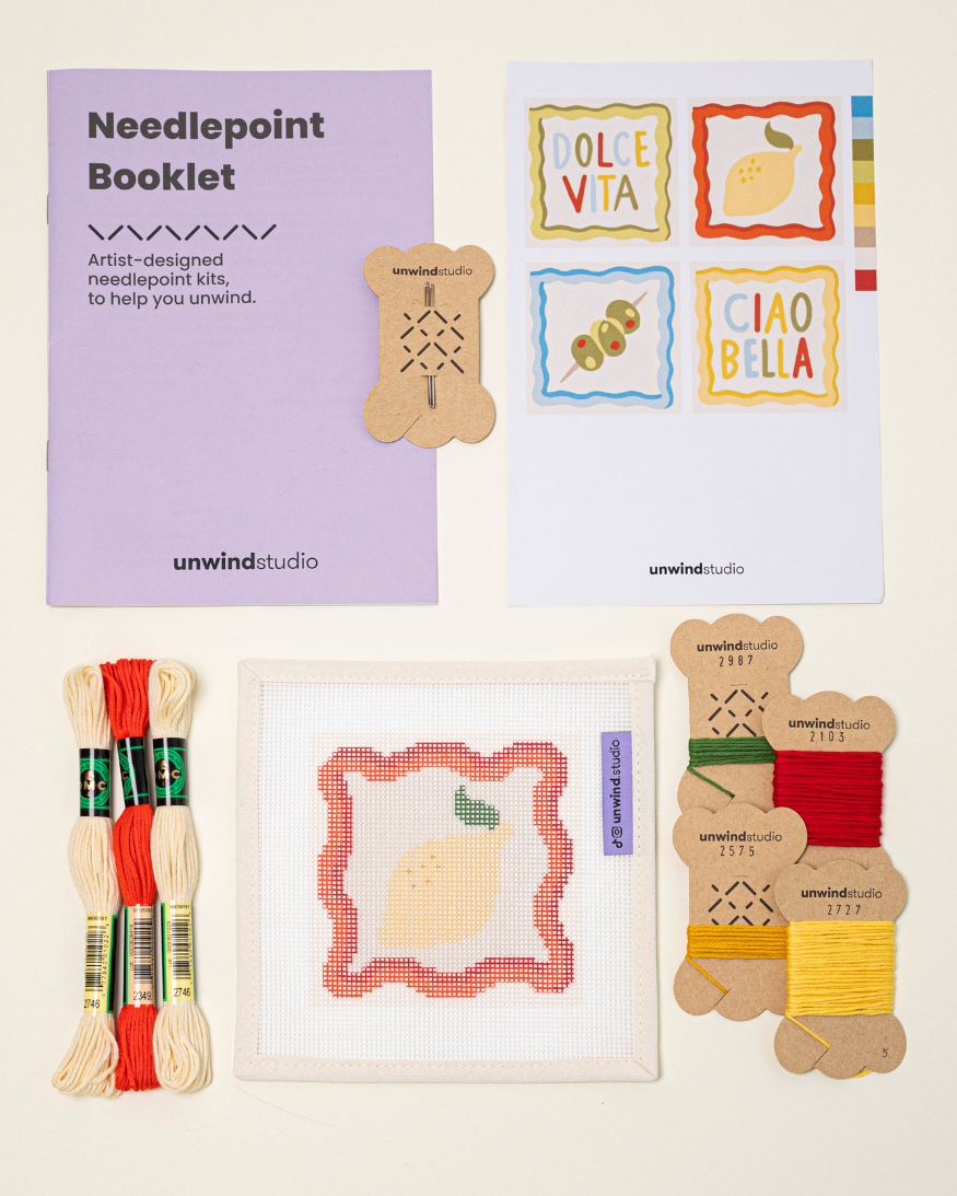 Top-down view of the limoncello spritz Coaster needlepoint kit including canvases, DMC Soft Cotton thread, flyer, and an instructional booklet.

