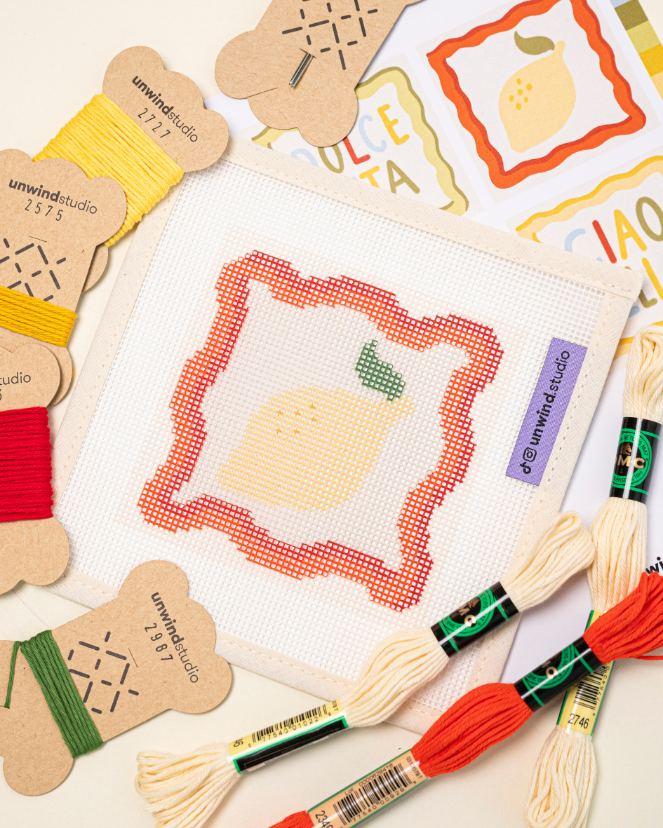 diagonal view of the unwind studio limoncello spritz needlepoint coaster with bold colorful threads.