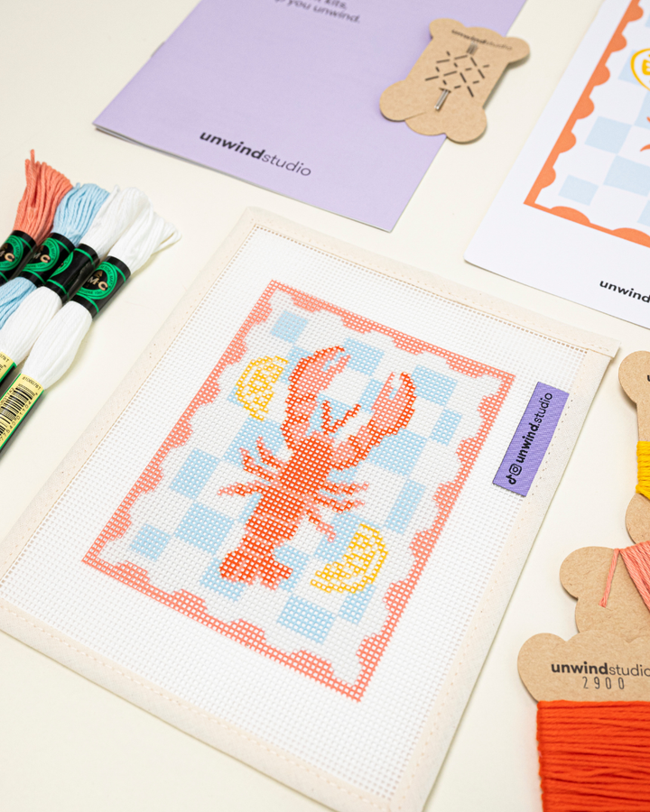 diagonal view of the unwind studio lobster needlepoint stamp with bold colorful threads.